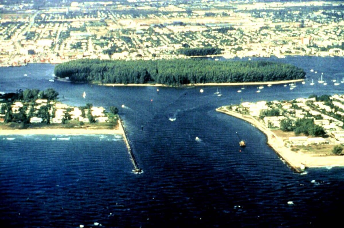 Aerial view west through the Lake Worth Inlet jetties toward Peanut Island, with Palm Beach Shores on Singer Island to the right
